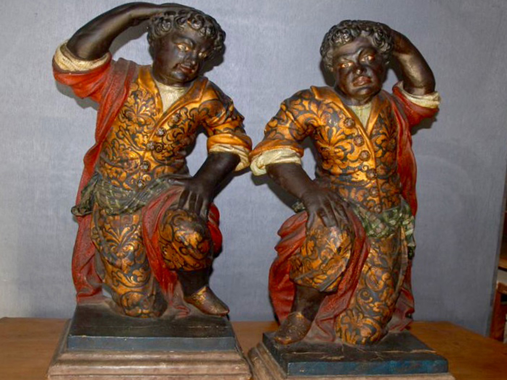 Cortonantiquaria 2015. Coppia di Moretti Veneziani del primo quarto del Secolo XVIII°. Il nome e la foggia, derivano dal termine moro che all'epoca denotava i musulmani o, per estensione, i pirati saraceni. In legno ebanizzato policromo, si presentano nella loro veste luminosissima incisa e dorata. Non portano copricapo ma poggiano rispettivamente la mano destra e sinistra sui fitti capelli ricci e finemente intagliati. Indossano calzari colorati. La posa speculare di gambe e braccia fa pensare che i due Moretti siano stati creati per essere collocati l'uno dirimpetto all'altro o comunque in posizione opposto. Altezza cm. 54.