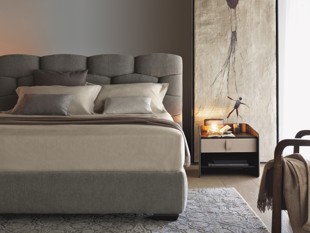 Flou. Letto matrimoniale Majal. Design Carlo Colombo. Il tessuto è l'elemento predominante nelle forme geometriche della grande e morbida testata. Il piano di riposo è a doghe regolabile ma disponibile anche con rete a movimento elettrico. Il rivestimento è in tessuto o pelle sfoderabile.