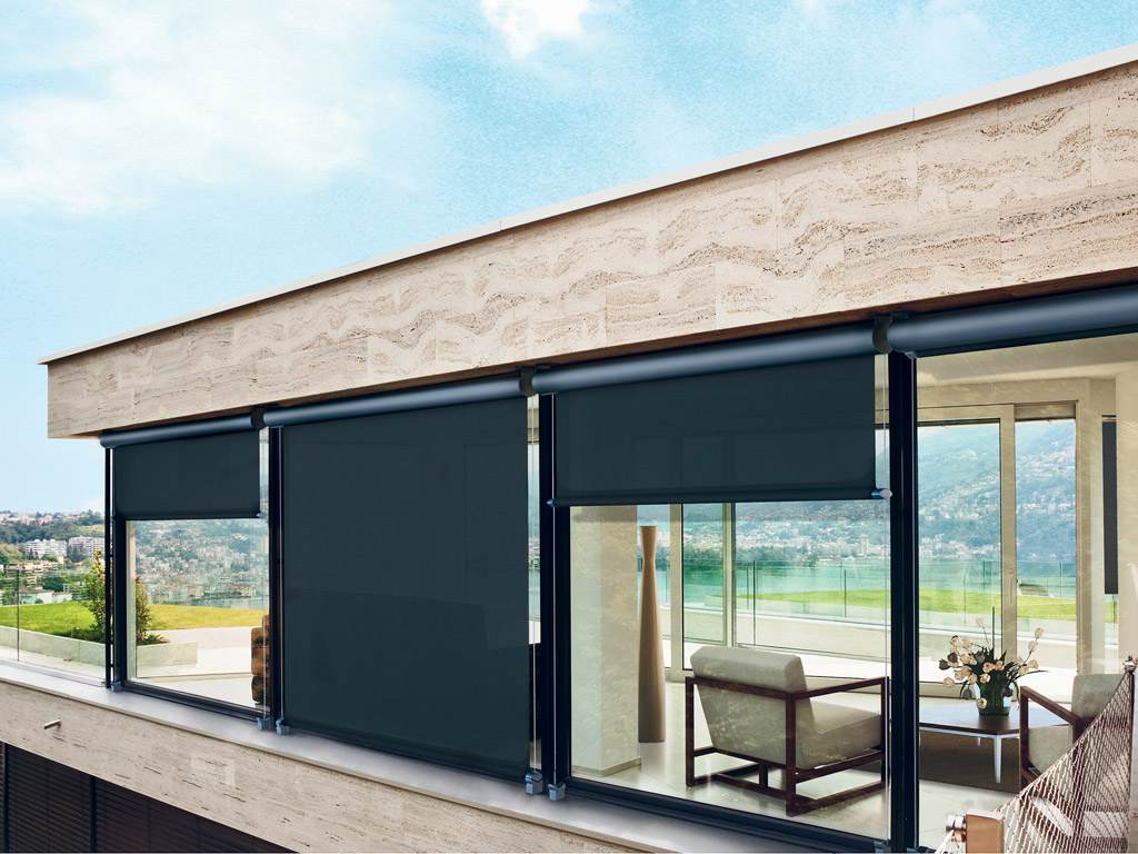 Pratic. “T-Line”, tenda a rullo verticale a cassonetto con telo guidato da cavi laterali. L’esclusivo aggancio Magnetic Lock System®, brevetto europeo di Pratic, permette il costante tensionamento del telo della tenda anche in presenza di brezze sostenute.