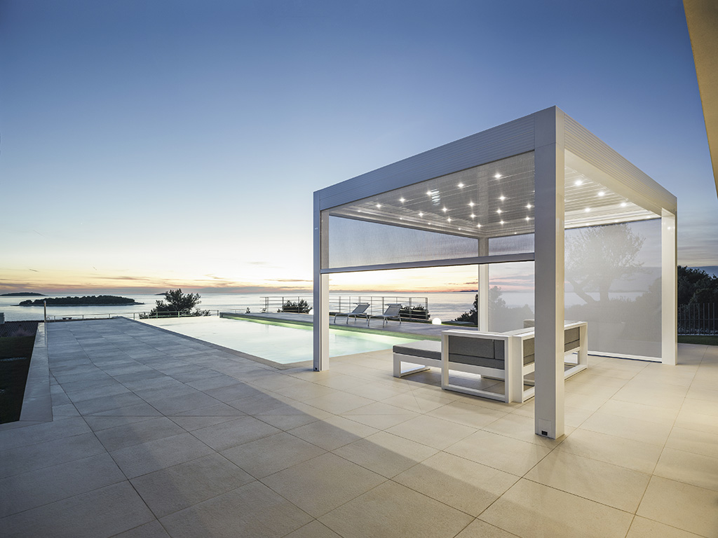 Gibus. La struttura in alluminio della pergola bioclimatica “Med Varia” integra completamente le chiusure avvolgibili Zip all'interno dei profili. Permette l’accoppiamento sui lati di chiusure vetrate, o teli screen ombreggianti.