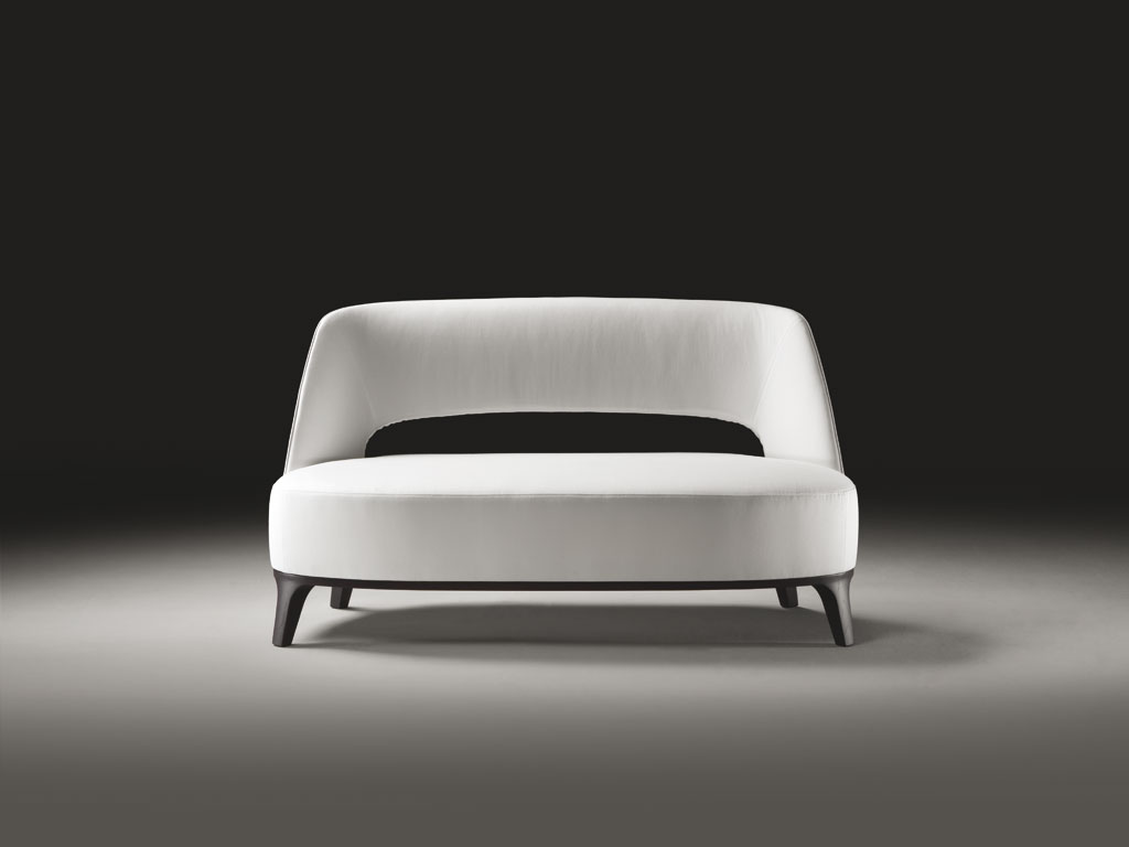 Flexform. “Ermione”. Divanetto basso su base in legno si affianca alla già nota poltrona. Presenta il caratteristico schienale imbottito che lascia una grande fessura aperta sopra il cuscino di seduta dall'altezza importante. Proporzioni garbate e aspetto solido ma leggero. Design Roberto Lazzeroni, collezione Flexform MOOD.