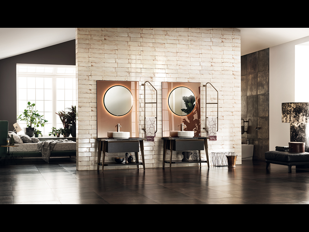 Scavolini Bagno. Nell’immagine, ambiente bagno arredato con il programma Diesel Open Workshop di Scavolini, realizzato in collaborazione con Diesel. Una delle peculiarità del programma Diesel Open Workshop è rappresentata dai grandi pannelli a specchio Stopsol effetto rame che fungono da quinta al mobile bagno. Le basi lavabo, qui presentate nella versione in Laccato Opaco Nero Ardesia, sono completate da un altro elemento estetico di forte connotazione del modello: il tubolare porta salviette, ovvero la struttura dell’elemento del Sistema Stock Rack reinterpretata, girevole, per nuovi usi.