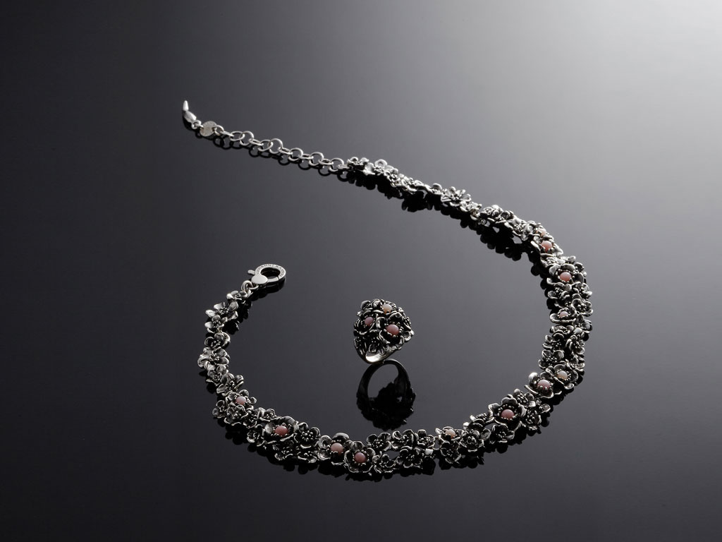 Giovanni Raspini. Collezione Wild Rose presentata con tre collane, tre bracciali, due orecchini e un anello. Argento brunito e opale rosa utilizzata con taglio cabochon in due dimensioni. Collezione Primavera Estate 2018.