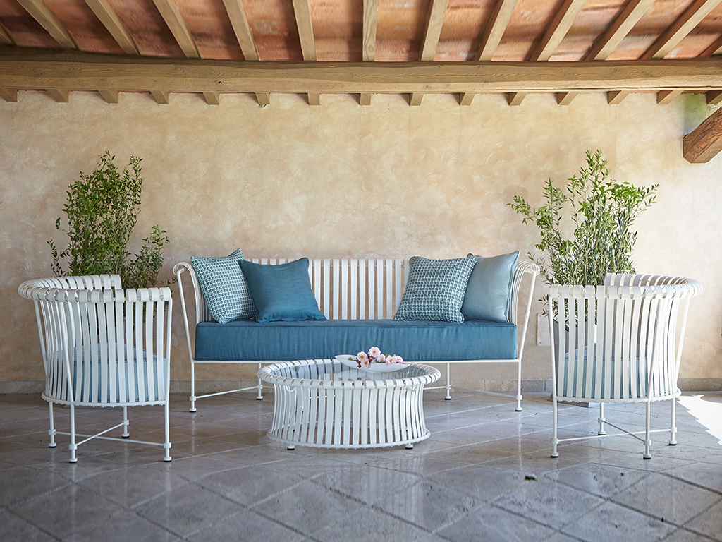 Officinaciani. La nuova collezione di arredi per esterni “Molle” è caratterizzata da una struttura decorativa in ferro piegato a mano, zincato e verniciato a polvere. Le sedute, disponibili nelle versioni divano a tre posti e poltrona, sono complete di cuscinerie realizzate con interni in gomma indeformabile e rivestite in tessuto outdoor Sunbrella. I tavolini bassi, realizzati in due misure, sono proposti con piano in cristallo.