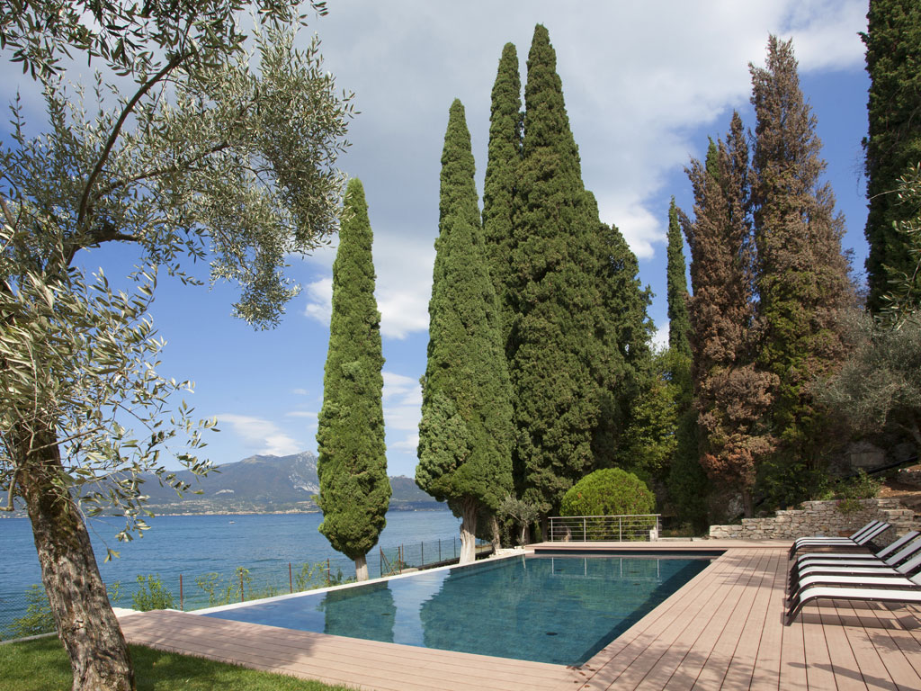 Isola Verde Piscine. Siamo all’interno di un parco che guarda sul Garda. La ristrutturazione di una villa di fine ‘800 e la riqualificazione di tutta l’area verde è stata l’occasione per inserirvi, con discrezione, una piscina realizzata con materiali antiriflettenti. In questo modo se ne è abbassato il grado di rifrangenza che avrebbe potuto determinare alterazioni dal punto di vista paesaggistico. La struttura della piscina è in lastre di acciaio, rivestita in Mortex® Etanche & Color, materiale impermeabilizzante, antiriflettente, a finitura opaca. I materiali lapidei della piscina sono in Giallo d’Istria e la zona relax è pavimentata con listoni in legno. Progettista: architetto Luigi Bruno.