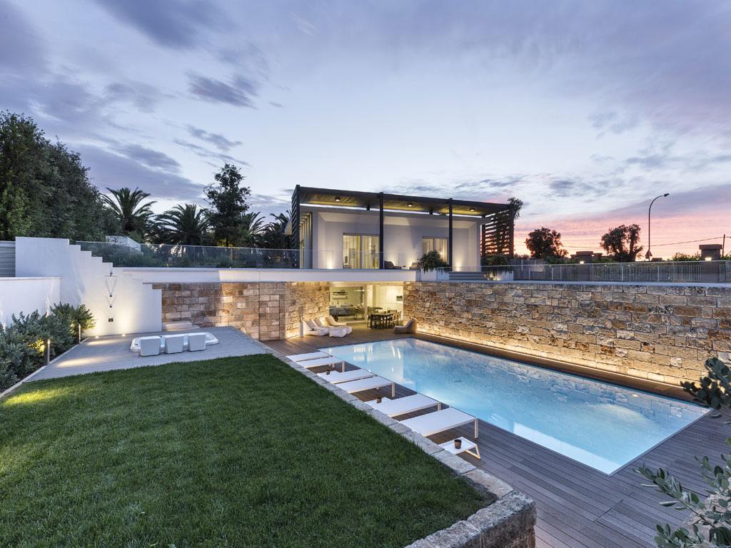 Piscine Castiglione. La villa, una “Casa Passiva” progettata dall’architetto Francesco Longano è immersa in un ampio spazio verde dove sono collocate una piscina, una minipiscina idromassaggio e un antico agrumeto. Per la realizzazione della piscina con bordo a sfioro, il concessionario Teknopiscine by M&D Group srl, ha utilizzato la tecnologia Myrtha®, fiore all’occhiello di Piscine Castiglione. La vasca - dimensioni 5 x12 metri - è caratterizzata dalla scalinata di accesso con ampio e confortevole prendisole a filo d’acqua, copertura motorizzata a tapparella e sistema automatico di trattamento dell’acqua mentre la pavimentazione circostante è stata realizzata in deck composito.