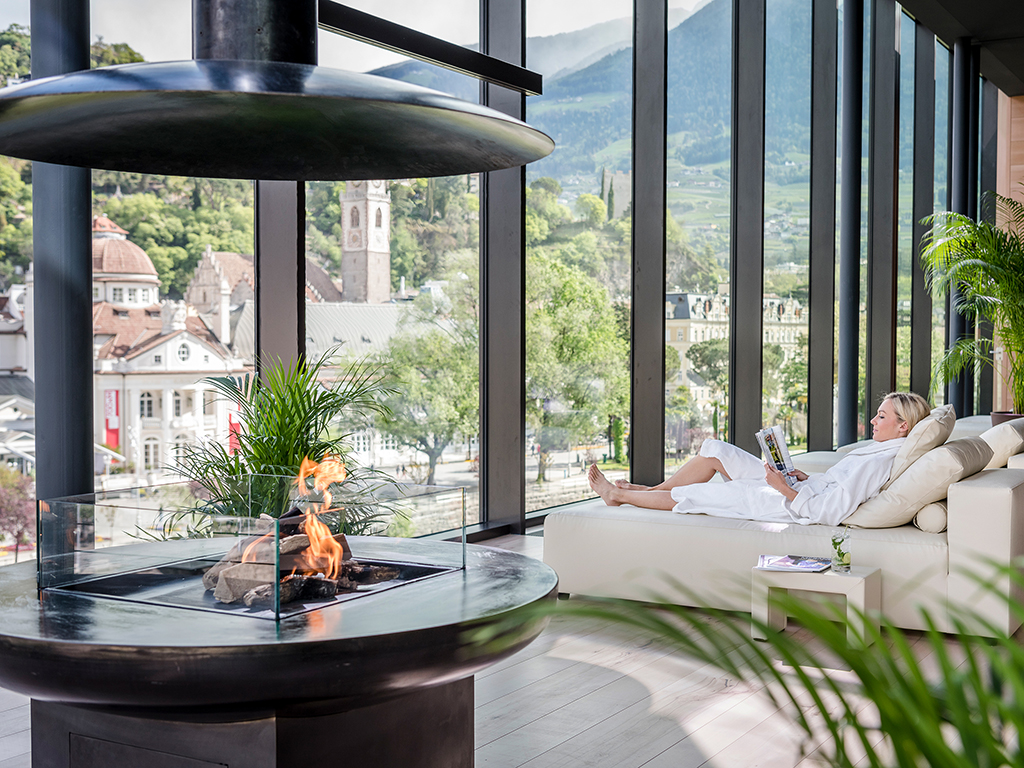 Hotel Terme Merano. Nell’immagine l’area relax della Sky SPA. Predomina il legno di cedro nobile ed è dotata di lettini confortevoli e accoglienti isole di ricreazione. L’atmosfera è rilassante e suggestiva anche grazie al fuoco scoppiettante del caminetto. Tutti i settori del centro benessere sono associati ad un elemento: le piscine e il bagno vapore all’acqua, la sala fitness e la sauna finlandese al fuoco, la sala relax e la sauna erbe alla terra, le terrazze panoramiche all’aria.