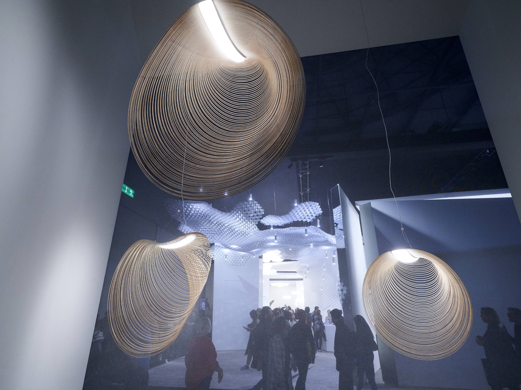 Luceplan. La lampada a sospensione “Illan” è una creazione della giovane designer ungherese Zsuzsanna Horvath. La leggerissima cornucopia è realizzata in multistrato di legno tagliato a laser secondo linee equidistanti e, una volta appesa, grazie alla gravità, genera una fluttuante forma organica. Al suo interno è collocata una sorgente LED per un'illuminazione diffusa e rilassante.
