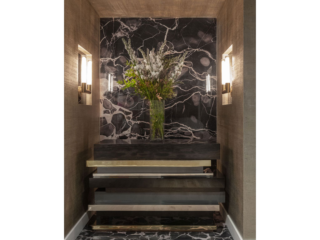 Benning Design Construction. Nell’ingresso: consolle in bronzo, acciaio inox e legno, posta su uno sfondo in pietra.