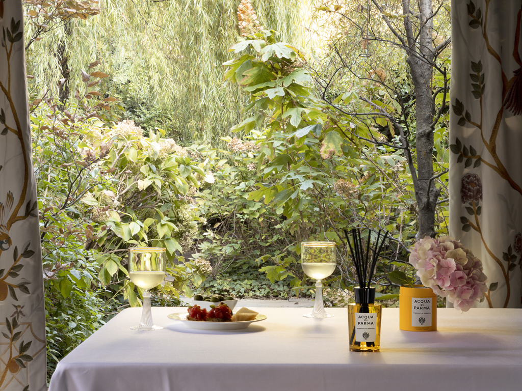 Acqua di Parma. Home Collection. Aperitivo in Terrazza. Proposto nella versione candela nel bicchiere da 200gr e diffusore da 180ml. Il bicchiere, realizzato con uno stampo esclusivo, riproduce il flacone Art Déco di Colonia. Mentre il diffusore, sempre dalle linee Art Déco, completa il proprio design con l’iconico tappo e i bastoncini in rattan. Candela, euro 54,00. Diffusore euro 65,00.