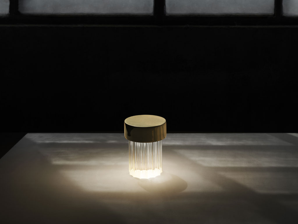 Flos. “Last Order” è una piccola lampada da tavolo (è alta circa 14 cm) portatile e ricaricabile. La luce che emana è diffusa attraverso una base in vetro solido trasparente, la cui forma richiama la tipologia architettonica della colonna greca. Il vetro è disponibile in due versioni: a superficie liscia, o scanalata (nella foto). La copertura è disponibile in diverse combinazioni di finiture metalliche e colorate: rame satinato e ottone per la versione da interni, inox lucido e verde opale verniciato per l’utilizzo in esterno. Fonte luminosa: LED 2,5W – 200lm – 2700K - CRI 90. Design Michael Anastassiades.