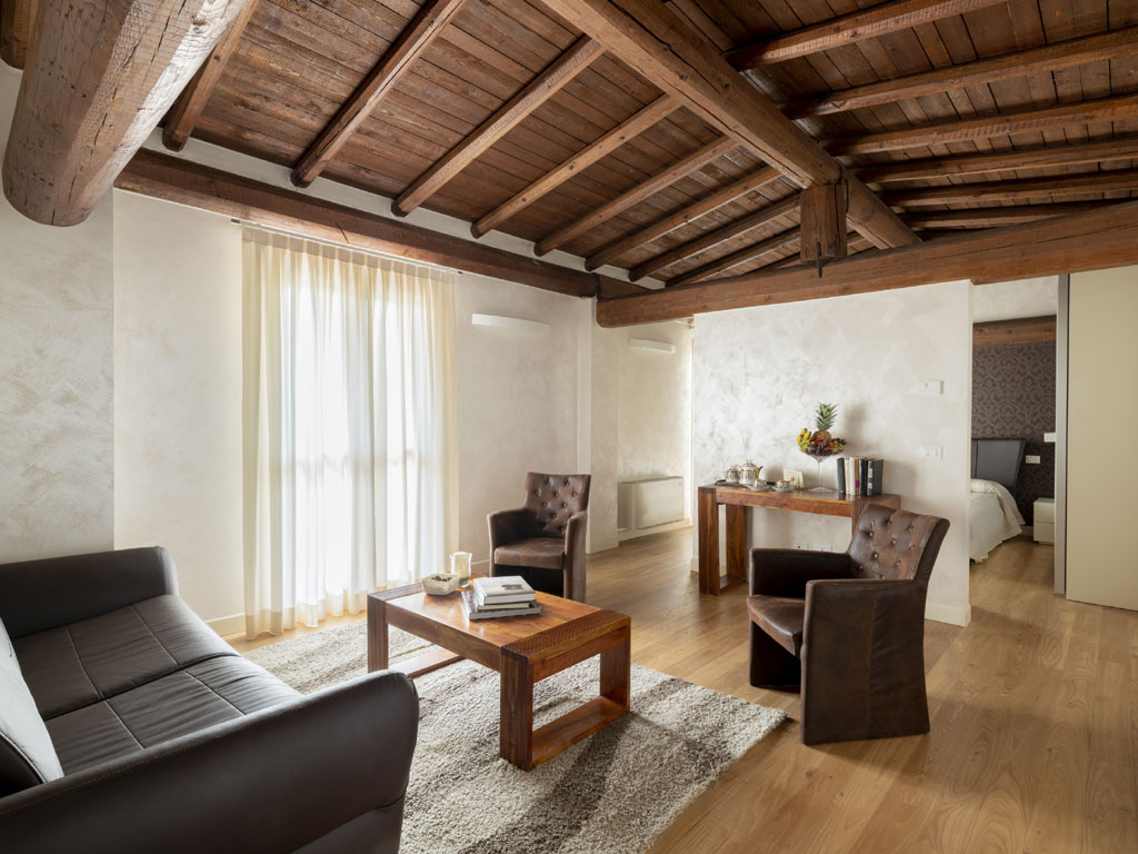 Agriturismo Corte Lantieri. Camera Nike. Suite matrimoniale, dedicata alla Dea della Vittoria, composta da camera e salotto con divano/letto. Grandi dimensioni, luminosa con doppio affaccio e balconata con vista panoramica su vigneti e colline. Soffitto con grandi travi in legno e arredi eleganti e moderni.
