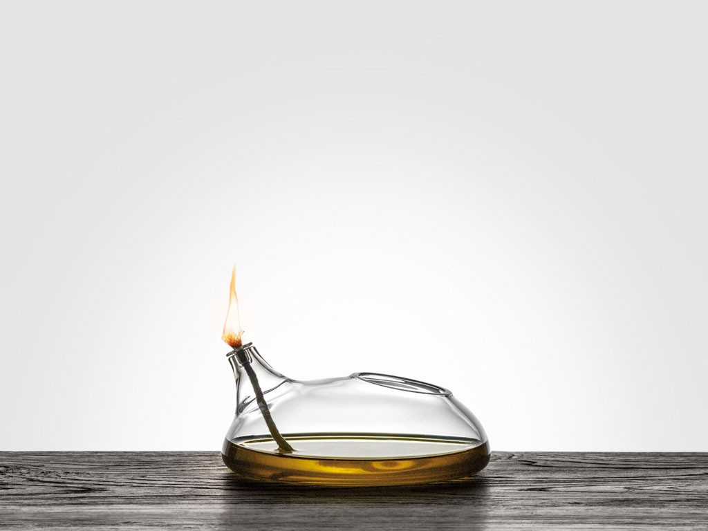 Blueside Emotional Design. “Lampara” evoca le lampade ad olio dell’antica Grecia. È alimentata con olio di oliva che per capillarità imbeve lo stoppino creando le condizioni per l’accensione. Fa parte della collezione di opere in vetro soffiato borosilicato “Le Nasse e l’olio”, progettata dall’architetto Simone Micheli. Dimensioni: 120x130 mm.