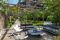 Italy Sotheby’s International Realty. Capri. L’ingresso alla casa è un lungo viale circondato da un pergolato di tronchi intrecciati. Al termine si apre un’area living intima e accogliente. Il giardino è disseminato di piante aromatiche, piante da frutto e viti.
